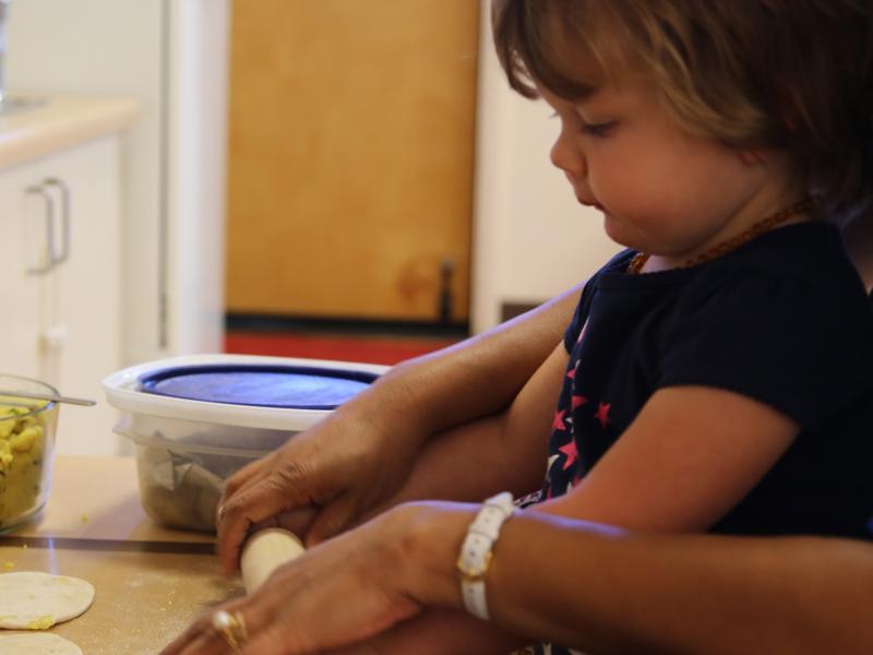 Toddler using a rolling pin while teacher guides her in a Montessori classroom