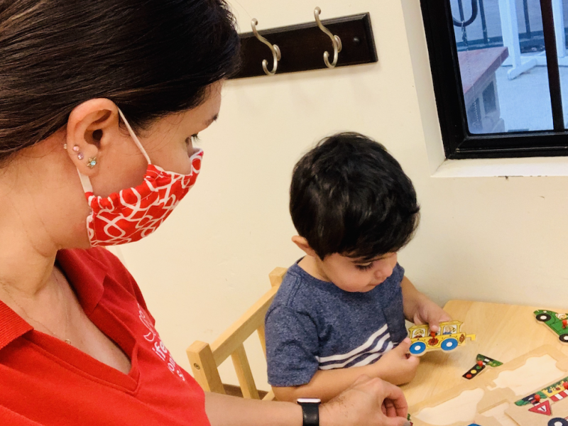 Toddler playing with puzzles while Montessori Teacher provides guidance