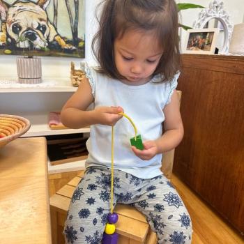 Toddler independently stringing beads in yarn at Lifetime Montessori School 